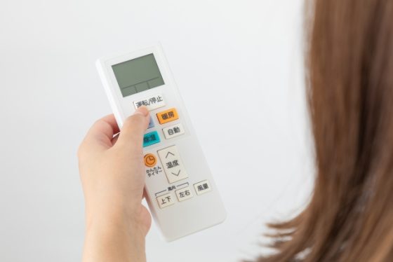 エアコンのリモコンを持つ女性